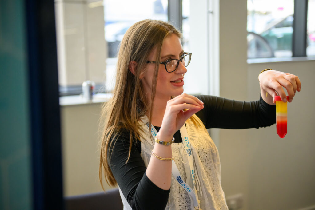 Researcher holding up a laboratory tube with coloured layers to discuss science with pupils.